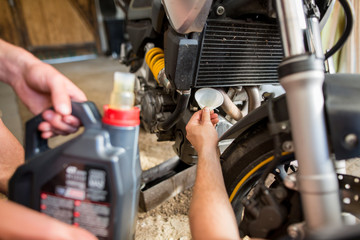 Mechanics changing the engine oil on motorbike, doing regular maintenance