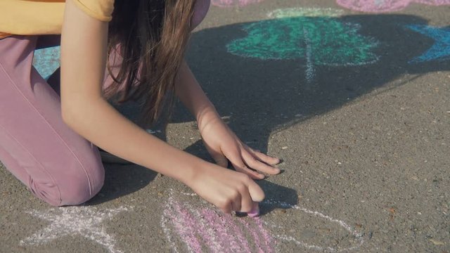 The child paints with chalk. A little girl draws a heart with chalk on the asphalt.