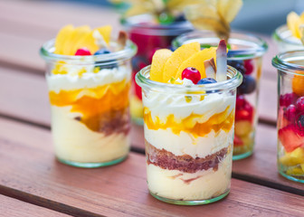 Dessert Nachspeise im Glas mit Crumble, Creme, Früchten, Mango, Biskuit au feinem Holztisch serviert auf einer Party vom Catering. schön angerichtet