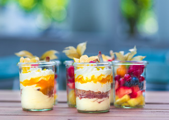 Dessert Nachspeise im Glas mit Crumble, Creme, Früchten, Mango, Biskuit au feinem Holztisch serviert auf einer Party vom Catering. schön angerichtet