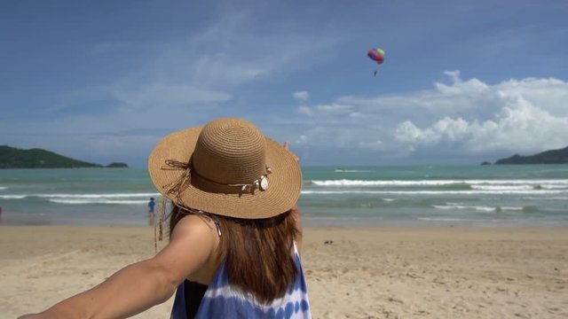 Young woman traveler holding man's hand and looking parachute flying in the sky on the beach, Couple vacation travel summer concept