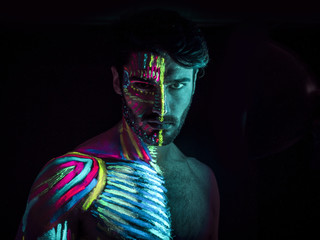 Young man painted in fluorescent paint on face and muscular torso, in studio shot with UV light