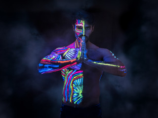 Young man painted in fluorescent paint on face and muscular torso, in studio shot with UV light