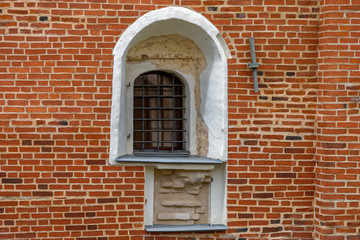 Arched window with iron grill on an ancient red brick wall.