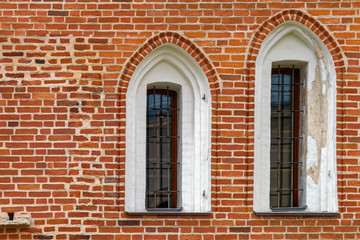 Arched windows with iron grill on an ancient red brick wall.