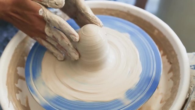 The hands of an amateur woman work with malleable wet clay on a potter's wheel to create a handmade crafted ceramic kitchenware