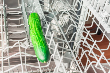 Long green cucumber lies in the middle compartment of the dishwasher