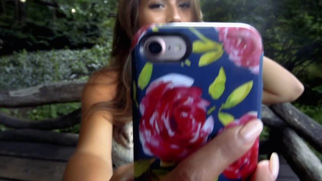 Young Caucasian Woman With Long Brunette Hair Sits On A Park Bench And Shots Snapchat Style Videos and Shares Them With You