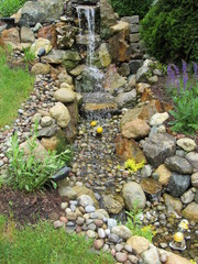 A man made waterfall and stream leading to a Koi fish pond at the bottom 