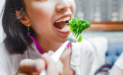 Portrait of happy smiling young casual woman eating broccoli in restaurant