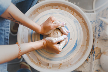 Top view of hands with clay making of a ceramic pot on the pottery wheel, hobby and leisure with...