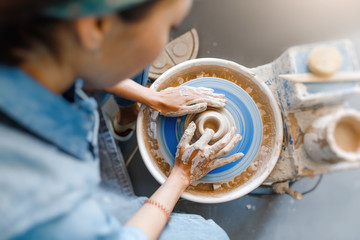 smiling woman making ceramic dishware on pottery wheel with clay, workshop and leisure concept