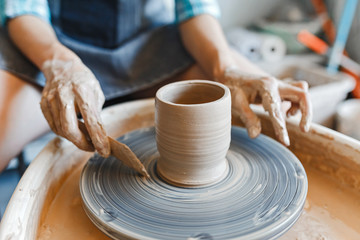 Top view of hands with clay making of a ceramic pot on the pottery wheel, hobby and leisure with pleasure concept - obrazy, fototapety, plakaty