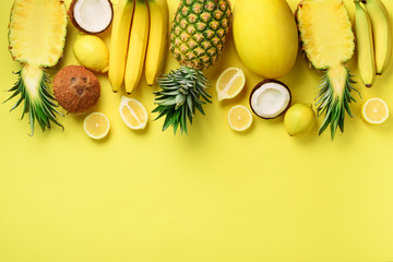Fresh organic yellow fruits over sunny background. Monochrome concept with banana, coconut, pineapple, lemon, melon. Top view. Copy space. Pop art design, creative summer design. Vegan food. Flat lay