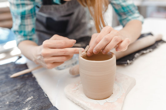 Close-up view of a female potter making and molding clay dishware in a workshop using different tools