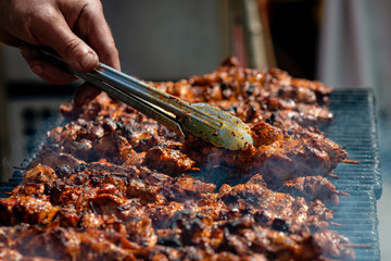 Meat on skewers fried on the grill in the open air, visible hands of the cook.