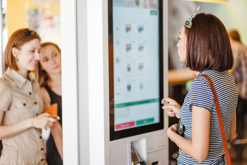 Group of people, friends ordering food at the touch screen self service terminal by the electronic...