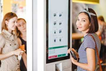 Group of people, friends ordering food at the touch screen self service terminal by the electronic menu in the fastfood restaurant