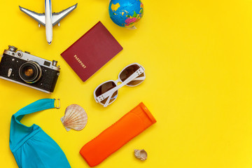 Flat Lay with Bikini, plane, vintage camera, passport, sunscreen, sunglasses and shell on yellow colourful trendy modern fashion background. Vacation travel summer weekend sea adventure trip concept