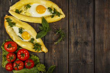 Khachapuri with fresh vegetables caucasian kitchen, close-up on a black wooden table. Adzharian khachapuri. View from above
