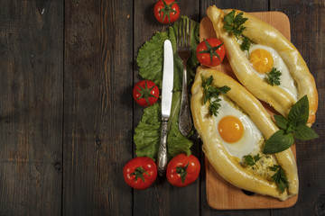 Khachapuri with fresh vegetables caucasian kitchen, close-up on a black wooden table. Adzharian khachapuri. View from above

