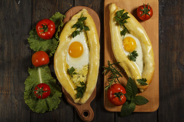 Khachapuri with fresh vegetables caucasian kitchen, close-up on a black wooden table. Adzharian khachapuri. View from above
