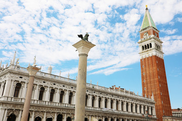 Fototapeta na wymiar White clouds in the blue sky on St. Mark square with bell tower and lion statue in Venice, Italy