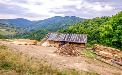 Old improvised sawmill on a mountain peak with a lot of timber and lumber laying around in piles and green trees on the back