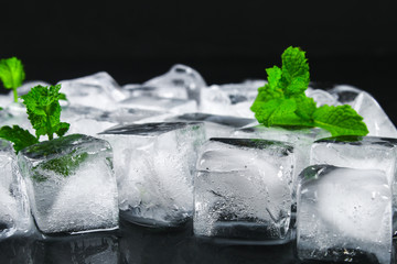 Cubes of ice from water with mint leaves on a black background.