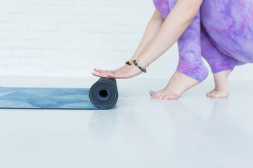 Close-up on hands yoga woman rolling her blue mat after a yoga class on white floor, copy space