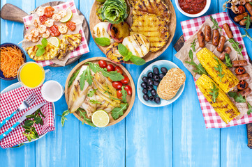 Grilled vegetables, shrimp, fruit on a wooden plate and sausages, juice and salad on a blue background. Summer dinner. Free space for text. Copy space.