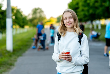 Girl schoolgirl. Summer in nature. Pose close up. Free space for text. He holds a glass of coffee or tea in his hands. The concept of rest after institute. Emotions of happiness smiles.