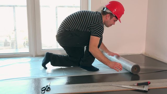 constructor man with red helmet lay underlay for laminate flooring installation