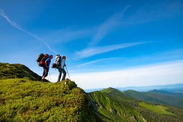 Adventurers with backpacks stands on green mountain ridge - Powered by Adobe