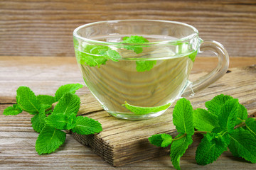 Fresh organic mint tea in glass on wooden table.