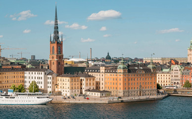 Fototapeta premium Sweden capital cityscape with tower of Riddarholm Church and touristic ship on water. Stockholm at sunny day