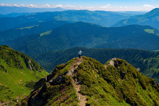 Adventurer female is standing on the green mountain ridge