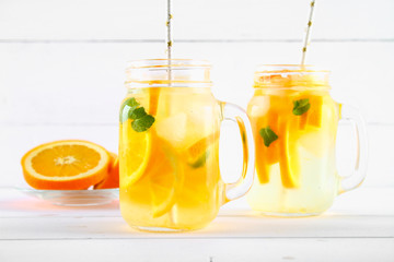 Orange detox water in mason jars on a white wooden table. Healthy food, drinks.