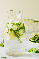 Lemonade with cucumber, lemon balm and thyme in a transparent jar on the background of plates with ingredients.