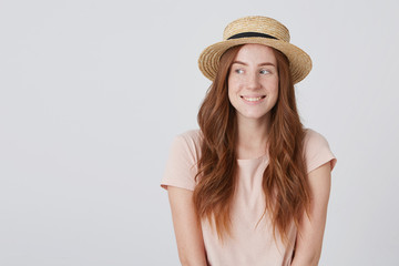 Closeup of smiling attractive young woman with long red hair in straw hat smiling and looking a side feeling happy over white background