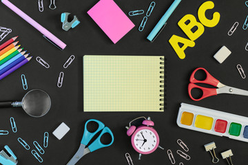 In the center of the black background is an empty notebook with a place for text. There are clerical and school supplies all around. Pictures on top, mock up.