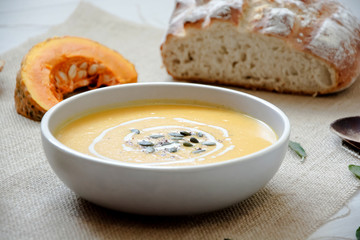Pumpkin soup with pumpkin seeds. In white bowl, on hessian fabric. With pumpkin slice, wooden spoon and wholegrain rustic bread. 