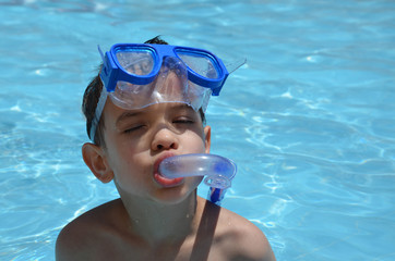 A happy young boy relaxing on the side of a swimming pool wearing blue goggles and snorkel