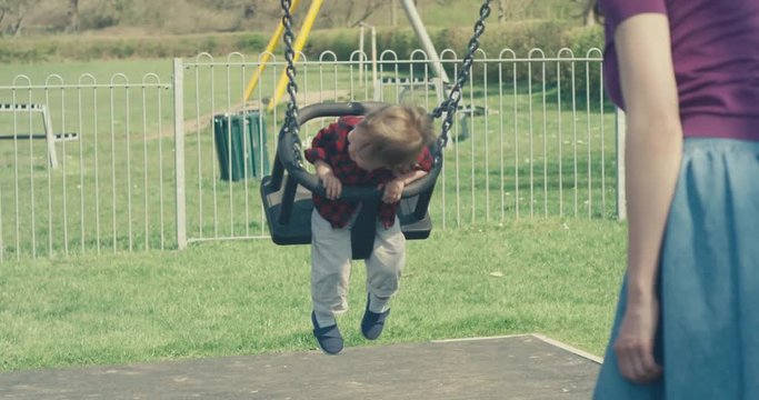 Young mother pushing her toddler boy on a swing
