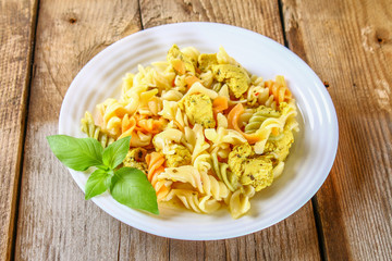 Pasta with slices of fried chicken fillet on an old wooden table.