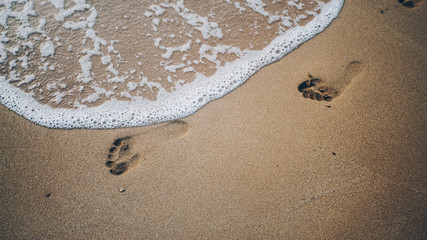 Two footprints on sand at the beach with waves and foam
