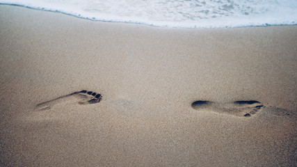 Two footprints on sand at the beach with waves and foam. CLose up