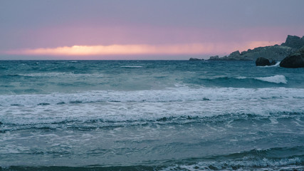 Beautiful pink and purple sunset on the beach. Sea, ocean with waves at dusk.
