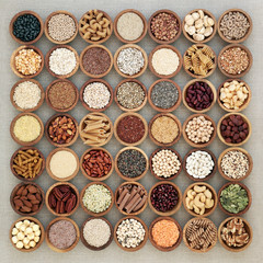 Vegan high protein dried health food with nuts, seeds, legumes, whole wheat pasta, grains & cereals. Foods high in fibre, antioxidants, anthocyanins, vitamins & minerals. Top view on hessian.