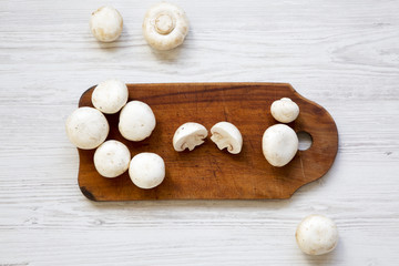Champignon mushrooms on wooden board. White wooden background. From above.